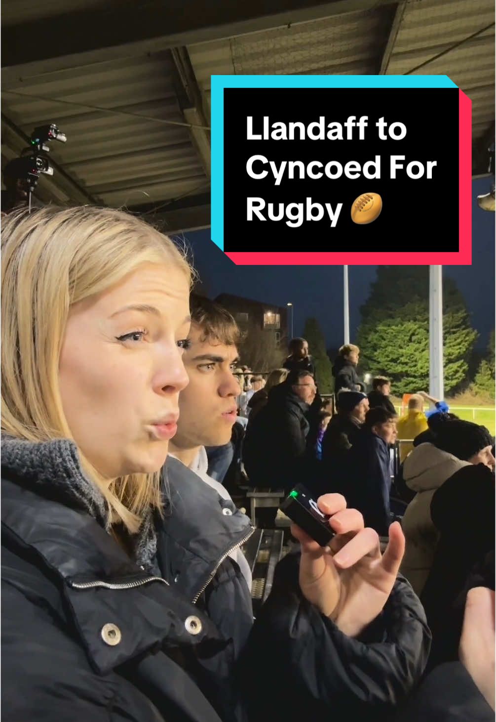 A young woman holding a lapel microphone sits in the stands of a sports stadium, next to a text box that reads 'Llandaff to Cyncoed for Rugby'