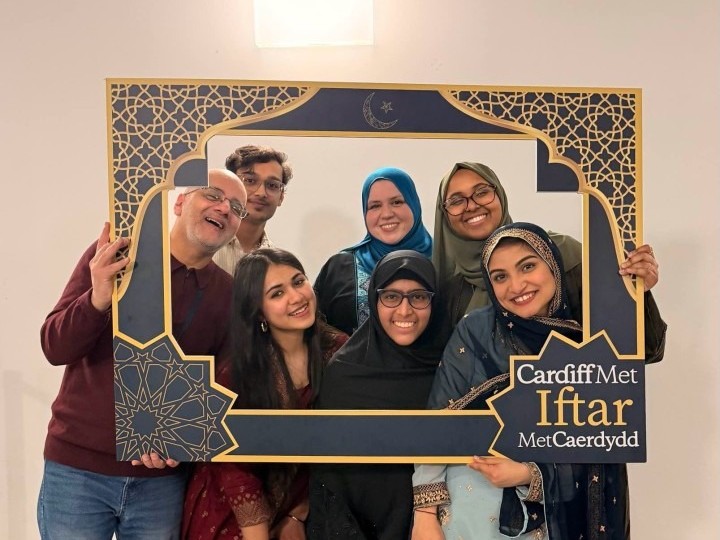 A group of people pose for a photo holding a decorative frame. In the corner of the frame is written Cardiff Met Iftar.
