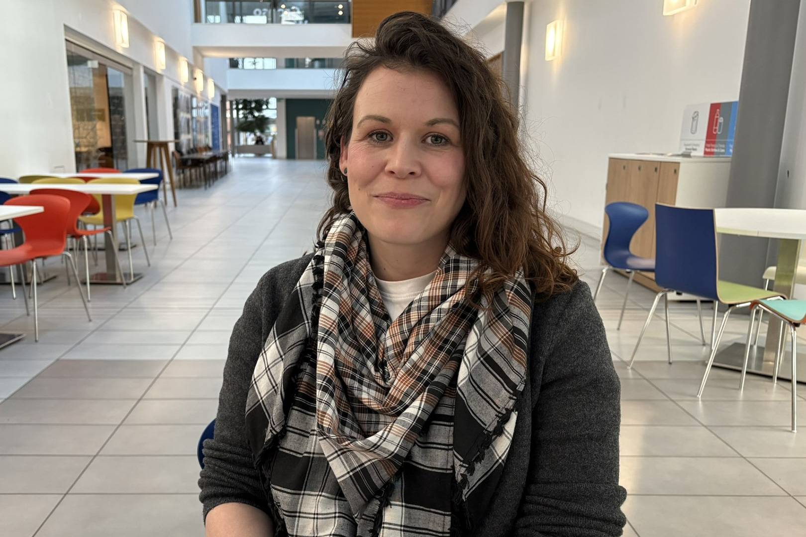 A woman wearing a scarf sits in the atrium at Cardiff School of Management.