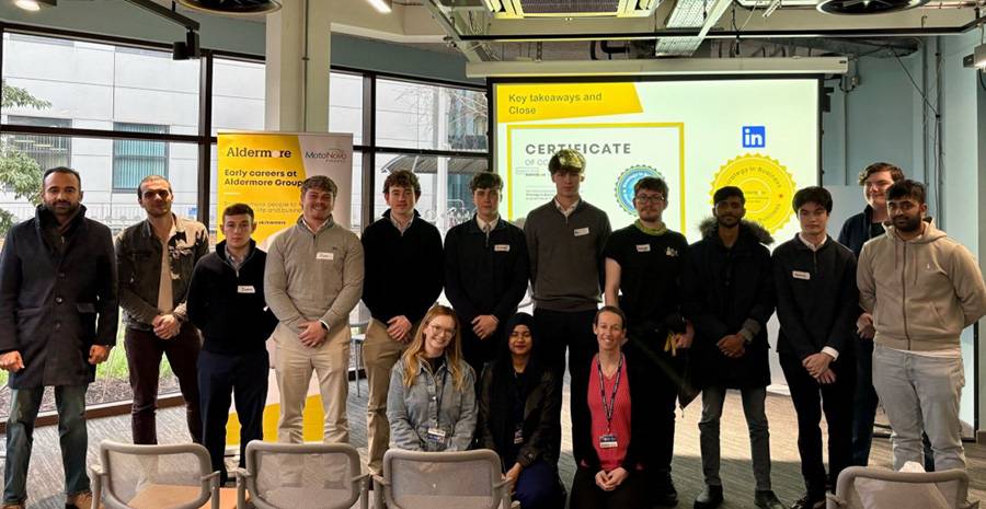 A group of people stand in a room with floor to ceiling windows. In the background, a certificate is shown on a projector screen.